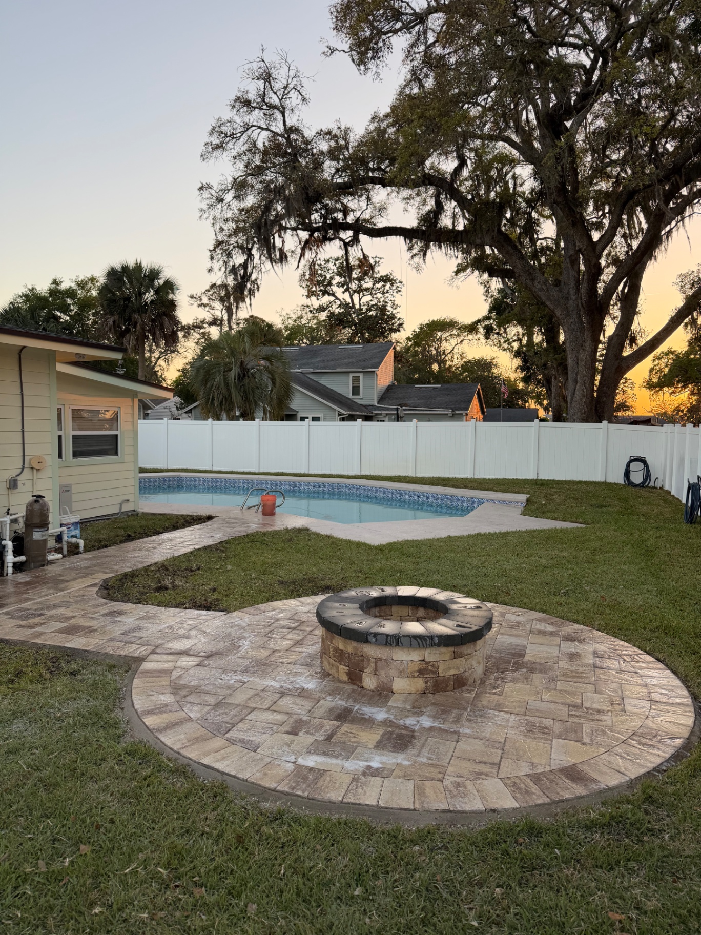 Circular paver patio with stone fire pit beside in-ground pool at sunset