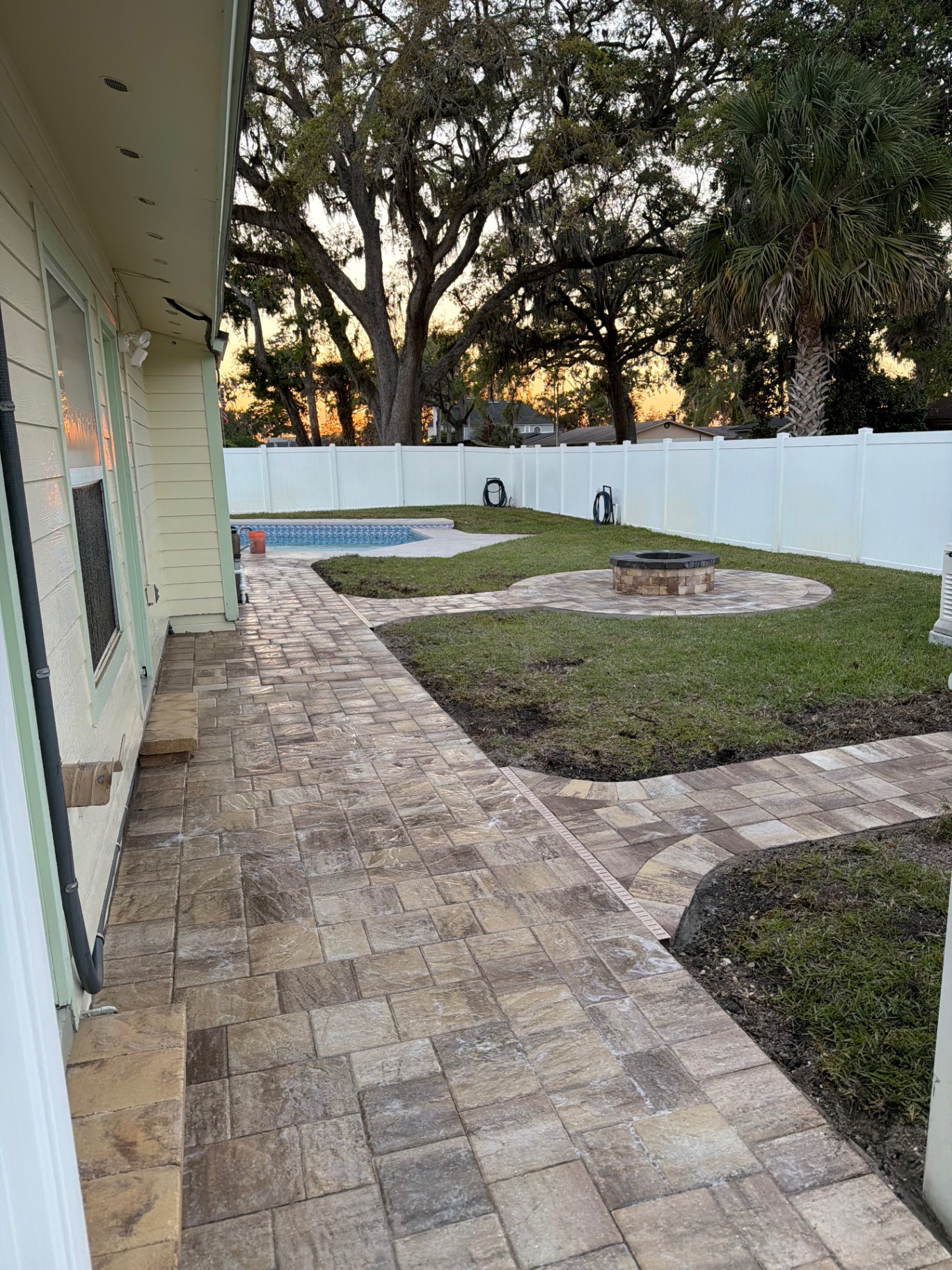 Wide paver walkway running alongside a home leading to pool and fire pit area