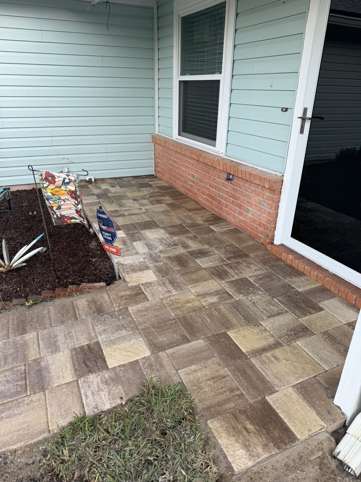 Paver walkway running alongside a house with brick foundation